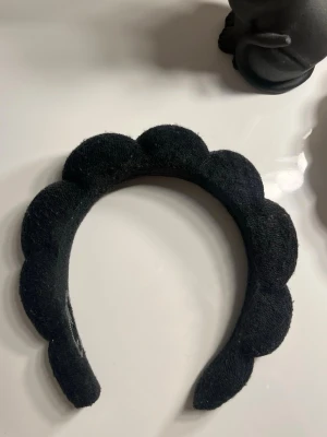 Svart scallop-format diadem - Säljer ett svart diadem med scallop-formad kant. Diademet är klätt i ett mjukt tygmaterial som ger en trendig och unik look. Perfekt accessoar för att lyfta din outfit med en cool twist.