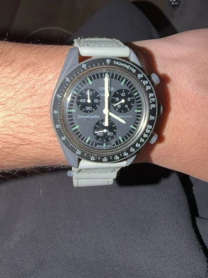 Swatch Mission to Mercury klocka - Snygg Swatch Mission to Mercury klocka med grå boett och matchande grått band. Klockan har tachymeter-skala runt urtavlan och två knappar på sidan för kronograf-funktion. Bandet är i syntetmaterial och har en modern, sportig look.