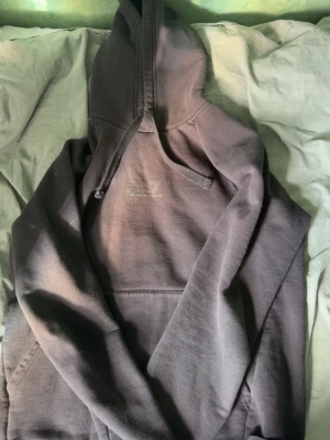 Mörkgrå hoodie från Emporio Armani - Snygg mörkgrå hoodie från Emporio Armani EA7 med broderad logga på bröstet. Klassisk modell med huva och dragsnören samt stor magficka framtill. Tillverkad i mjukt bomullsmaterial som känns skönt mot huden. Perfekt för en avslappnad och trendig look.