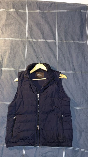 Mörkblå väst från Oscar Jacobson - Hej! Jag säljer en mörkblå väst från Oscar Jacobson. Den är i storlek xs, och passar perfekt som ett extra lager under jackan nu under våren. Jag köpte den för 2000kr, och säljer den nu för 750kr.