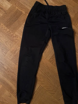 Svarta adidas mjukisbyxor Primeblue - Säljer ett par svarta mjukisbyxor från adidas med diskret logga på benet. Byxorna är tillverkade i Primeblue-material med Parley Ocean Plastic och har resår i midjan samt muddar vid bensluten. Perfekta för chill eller träning.