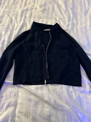 Mörkblå cardiganjacka med dragkedja - Stilren mörkblå cardiganjacka med krage och två stora bröstfickor. Kan användas som jacka eller kofta. Jag har använt den som kofta inomhus och jacka när det är varmt 
