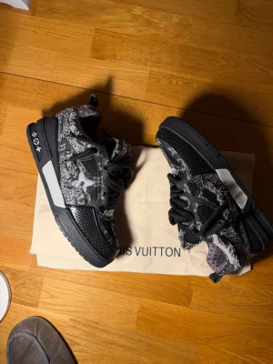 LV skate swarofski  - Unika Louis Vuitton sneakers i svart och grått med coolt mönster och fransade detaljer. Skorna har tjocka svarta snören, LV-logga på sidan och robust sula. Materialmix av textil och läder ger en lyxig känsla. Perfekta för dig som vill sticka ut.