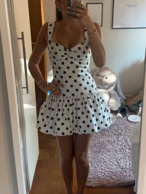Zara prockig klänning - Supersöt vit kort klänning med svarta prickar och volangkjol. Klänningen har breda axelband, markerad midja och en lätt v-ringad byst med twistad detalj framtill. Perfekt för sommarens alla tillfällen!