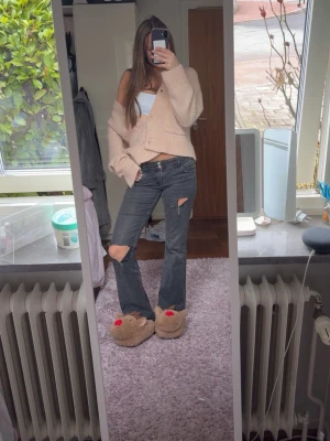 Grå slitna bootcut jeans - Säljer ett par grå bootcut jeans med slitningar och hål vid knäna. Jeansen har låg midja och klassiska fem fickor. Perfekta för en avslappnad och trendig look. Inget synligt märke på jeansen.