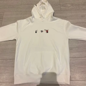 Off-White Vit hoodie - Säljer en stilren vit hoodie från Off-White med en unik grafisk design på ryggen i svart och rött. Framsidan har en diskret logotyp i samma färger. Perfekt för dig som vill ha något trendigt och bekvämt.