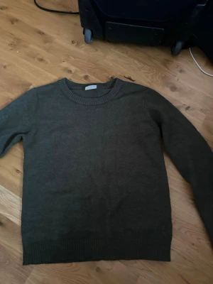 Mörkgrön stickad tröja från Vila - En enkel och stilren mörkgrön stickad tröja från Vila. Tröjan har rund halsringning, långa ärmar och ribbade muddar vid ärmslut och nederkant. Perfekt att matcha med jeans eller kjol för en avslappnad look.