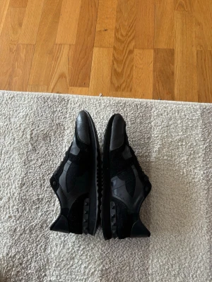 Svarta sneakers från Valentino - Snygga svarta sneakers från Valentino med kamouflagemönster och detaljer i mocka och läder. Skorna har svarta snören, låg profil och coola nitar på sulan. Perfekta för dig som vill ha en stilren men ändå unik look.