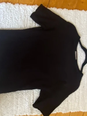 Svart stickad t-shirt i bomull - En enkel svart t-shirt med rund hals och korta ärmar. Tillverkad i mjuk bomull, perfekt för en clean och stilren look. Passar till allt och är ett måste i garderoben. Jättesnygg❣️❣️ Lite tightare runt midjan snyggt att ha på sommaren❣️❣️