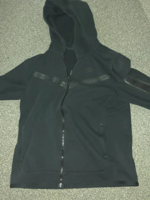 Svart Nike tech  - Svart Nike tech med hel dragkedja framtill och huva. Säljer för att den är liten. Det finns inga fläckar på den. Säljer även för vill ha pengar och vill bli av med den. Kan frakta inom 1-2 dagar 