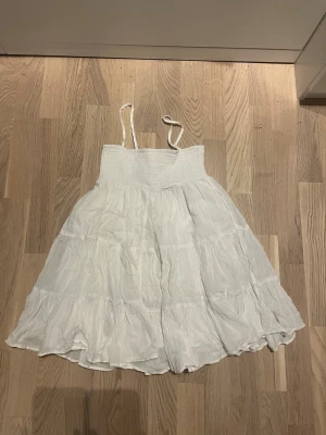 Vit sommarklänning med volanger - Luftig vit klänning med smala axelband och volangdetaljer. Klänningen har en smockad överdel och är tillverkad i ett lätt, skrynkligt tyg som passar perfekt för varma dagar.❤️