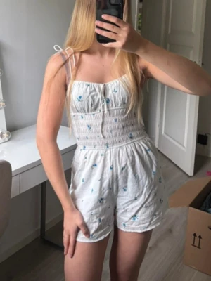 Kort blommig jumpsuit  - Använd vid något tillfälle, i stort sett som ny. Banden knyter man själv och anpassar efter sig själv.