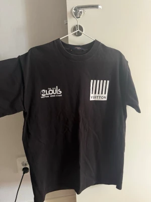 Svart Louis Vuitton t-shirt - Snygg svart t-shirt från Louis Vuitton med tryck fram i vitt och coolt grafiskt tryck bak i rött och blått. Klassisk passform med rund hals och korta ärmar
