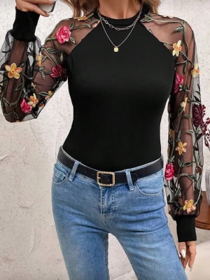 Svart topp med broderade meshärmar storlek XL - Trendig svart topp med transparenta meshärmar dekorerade med broderade blommor i rött och gult. Kroppsdelen är tight och enfärgad medan ärmarna har volym och muddar vid handlederna. Perfekt för dig som vill sticka ut lite extra.