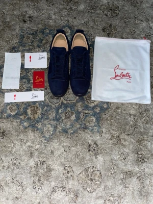 Mörkblå sneakers från Louboutin - Snygga mörkblå sneakers från Christian Louboutin i mocka med matchande mörkblå snörning och diskret logga på hälen. Skorna har en låg silhuett och klassisk design med exklusiv känsla. Perfekta för dig som gillar stilrena och lyxiga sneakers. Storlek 42