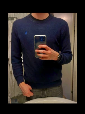 Mörkblå tröja från Polo Ralph Lauren - Klassisk mörkblå tröja från Polo Ralph Lauren med rund halsringning och diskret broderad logga i blått på bröstet. Perfekt för en stilren och enkel look. Storlek M