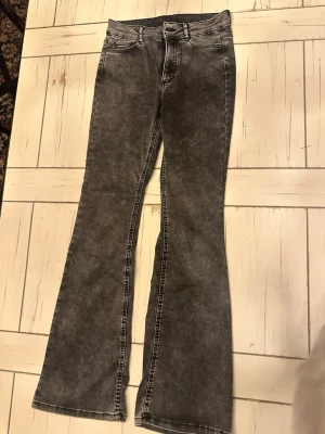 Grå bootcut jeans med tvättad look - Snygga grå jeans med bootcut passform och tvättad effekt. Klassisk femficksmodell med vita kontrastsömmar och hög midja. Perfekta för dig som vill ha en retro vibe i garderoben.