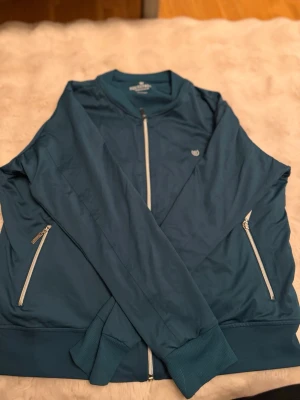 Grön  bomberjacka från Equestrian Stockholm - Snygg grön bomberjacka från Equestrian Stockholm med vita dragkedjor och ribbade muddar. Jackan har två fickor framtill och logga på bröstet samt stor text på ryggen. Tillverkad i ett lätt och mjukt material som ger en sportig look. Storlek L men upplevs som M/S💗aldrig andvönd