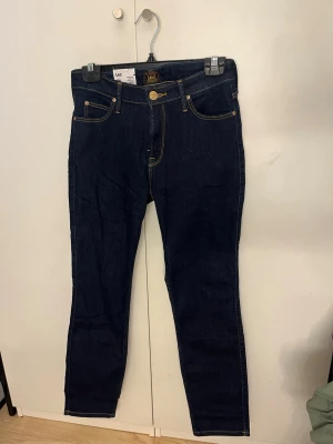 Mörkblå slim jeans från Lee - Snygga mörkblå slimade jeans från Lee med klassisk femficksdesign och kontrastsömmar i gult. Jeansen har hög midja och är tillverkade i stretchigt denimtyg för en bekväm passform. Perfekta till en avslappnad streetstyle-look. Nypris 999kr : 1000kr pris kan diskuteras!!😊