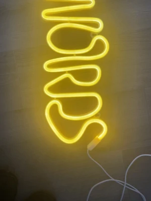 Gul neonlampa med texten WORDS - Säljer en cool neonlampa i form av ordet 'WORDS' i gul färg. Lampan har en modern, böjd design och drivs med sladd. Perfekt som dekoration till rummet eller kontoret för en unik vibe.