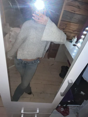 Grå croppad stickad tröja - Säljer en grå, croppad stickad tröja med breda ärmar och ribbstickad struktur. Tröjan har en avslappnad passform och är perfekt för lager på lager. Materialet känns mjukt och mysigt, perfekt för kyligare dagar.