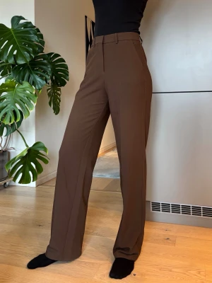 Bruna raka kostymbyxor - Bruna kostymbyxor med hög midja och raka ben. Byxorna har bälteshällor och pressveck framtill för en clean look.