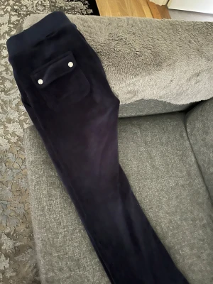 Mörkblå leggings från Juicy Couture - Snygga mörkblå leggings från Juicy Couture i mjuk velour. Modellen har en ficka bak med silverfärgade knappar och en tight passform. Perfekta för en chill och trendig look.