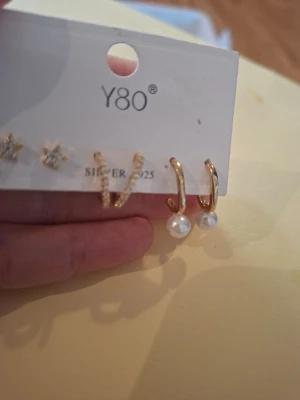 Set med örhängen  - Snyggt set med fyra par örhängen från Y80. Innehåller stjärnformade örhängen med stenar, små hoops med gnistrande detaljer samt guldiga hoops med hängande vita pärlor. Materialet är guldtonad metall och vissa delar i silver 925.