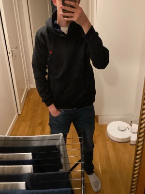 Svart hoodie från Ralph Lauren - Säljer en svart hoodie från Ralph Lauren med klassisk huva och känguruficka. Den har en liten röd broderad logga på bröstet och är perfekt för en chill och stilren look.