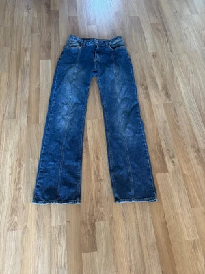 Blå raka jeans från okänt märke - Säljer ett par blå jeans med graze wide stil med raka ben och klassisk femficksdesign. Jeansen är mid-low waist och har tydliga sömmar längs benen. Perfekta för en avslappnad och trendig look.