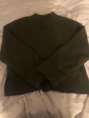Mörkgrön stickad tröja - Mysig mörkgrön stickad tröja med rund halsringning och breda ribbstickade muddar vid ärmslut och nederkant. Perfekt för lager-på-lager och enkel att matcha med jeans eller kjol.