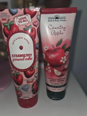 Bath & Body Works body creams - Två body creams från Bath & Body Works: Strawberry Pound Cake med jordgubbsdoft och Country Apple med äppeldoft. Tubformade förpackningar i rosa och rött med fruktmotiv. Innehåller sheasmör och hyaluronsyra för återfuktning.