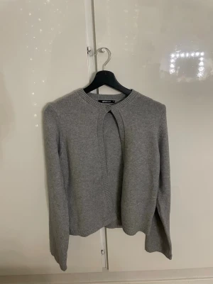 Grå kofta från Gina Tricot - Aldrig anvånd. En stilren grå kofta från Gina Tricot med rund halsringning och lång ärm. Koftan är stickad i mjukt material och har en enkel knäppning vid halsen. 