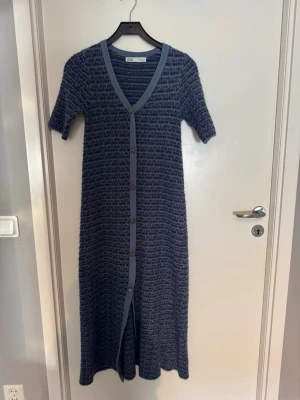 Marinblå långklänning från Zara - Långklänning från Zara i marinblått med korta ärmar och v-ringning. Klänningen har knappar hela vägen framtill och är stickad med ett diskret mönster. Perfekt för dig som gillar en avslappnad men stilren look.