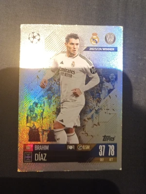 Topps Brahim Díaz samlarkort - Glittrigt samlarkort från Topps med Brahim Díaz i Real Madrids vita matchställ. Kortet har Champions League-märke, klubbmärke och spelarstatistik. Perfekt för dig som gillar fotboll och samlarkort.