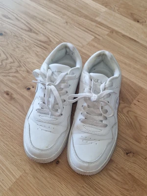 Sneakers - Vita sneakers strl 38 säljes. Endast använda ca 4–5 gånger då de tyvärr är för små för mig och gav skavsår. Därför är de fortfarande i väldigt fint skick utan fel eller skador. Har använt hälkuddar vilket lämnat lite limrester/märken vid hälen, men det går högst sannolikt att rengöra bort. Har även stått i källarförråd och kan behöva en lätt putsning, men annars är de fräscha och knappt använda.