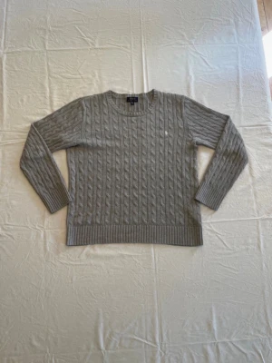 Grå kabelstickad tröja Polo Ralph Lauren - Kabelstickad tröja i ljusgrått från Polo Ralph Lauren. Tröjan har rund hals, långa ärmar och ribbade muddar. Materialet ser ut att vara mjukt och skönt, och den har en liten broderad logga på bröstet.                                                             Tveka inte, hör av er vid intresse, frågor eller prisförslag!
