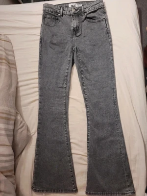 Grå bootcut jeans med broderade fickor - Säljer ett par grå bootcut jeans med snygga broderade detaljer på bakfickorna. Jeansen har klassisk femficksdesign, bälteshällor och dragkedjegylf. Perfekta för dig som gillar en lite vidare passform nertill.