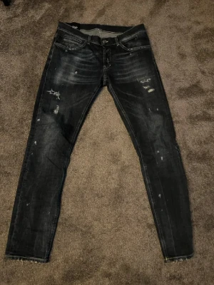 Mörkblå slitna slim jeans från dondup  - Säljer ett par mörkblå slim fit jeans från dondup med slitningar och distressed detaljer på benen. Jeansen har fem fickor, låg midja och smal passform. Perfekta för en trendig och avslappnad stil.