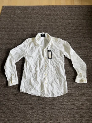 Vit skjorta från Jack & Jones - Klassisk vit skjorta från Jack & Jones med lång ärm och knappar framtill. Skjortan har en stilren krage och är tillverkad i ett lätt och bekvämt material, perfekt för en clean och enkel look.
