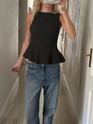 Mörkgrå topp från Zara - Snygg svart topp med ärmlös och figurnära passform. Toppen har en markerad midja och utsvängd nederdel som ger en feminin siluett. Perfekt att styla med jeans eller kjol för en trendig look.