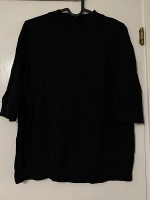 Svart finstickad tröja med 3/4-ärm från Cubus - En svart oversized tröja med 3/4-ärm och rund hals. Lite högre i kragen. Tröjan har en enkel och stilren design utan synliga detaljer eller mönster. Perfekt för dig som gillar en avslappnad och minimalistisk look.