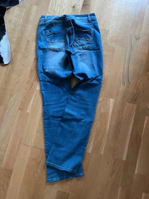 Blå bootcut jeans med fickdetaljer - Snygga blå bootcut jeans med klassiska fickor bak och ljusa slitningar framtill. Jeansen har normal passform och är perfekta för en avslappnad men ändå trendig look. Tillverkade i mjuk bomull som känns skön hela dagen.