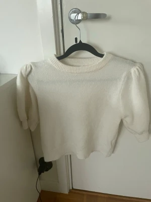 Vit stickad tröja från Gina Tricot - Säljer en söt vit stickad tröja från Gina Tricot med puffärmar och ribbstickad halsringning. Tröjan har en klassisk rak passform och är perfekt för att hålla sig varm under kyliga dagar. Enkel att matcha med olika outfits.