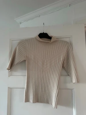 Beige ribbstickad topp med halvpolo från Lindex - Säljer en beige ribbstickad topp med halvpolo och trekvartsärm. Väldigt skönt och stretchig .