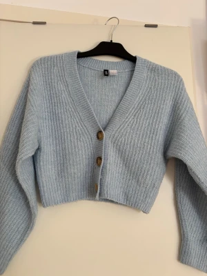 Ljusblå cropped kofta med knappar - Mysig ljusblå stickad kofta med tre bruna knappar framtill. Koftan är cropped och har en V-ringning eller off shoulder (kan användas till båda) samt långa ärmar. 💗