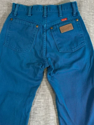 Vintage USA-made Wrangler 14MWZ high waist jeans in a rare teal blue colorway - Vintage USA-made Wrangler 14MWZ high waist jeans in a rare teal blue colorway. Classic western straight leg fit with rigid denim, copper hardware, and signature Wrangler patch. Perfect rugged Americana / Y2K vintage look with a super flattering high-rise cut.  Tagged 5/6 x 32 but fits approx women’s W25/W26.  Measurements laid flat: Waist: 32.5 cm Rise: 30 cm Thigh: 28 cm Knee: 21 cm Foot opening: 18 cm Inseam: approx. 79–80 cm Full length: approx. 108 cm  Good vintage condition with normal wear