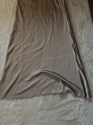Beige satin långkjol - Snygg beige långkjol från Lindex i glansigt satinmaterial. Kjolen har en rak och elegant siluett som ger en stilren look. Perfekt att matcha med en enkel topp eller stickad tröja för en trendig outfit. Kjolen är andvänd 2 gånger 