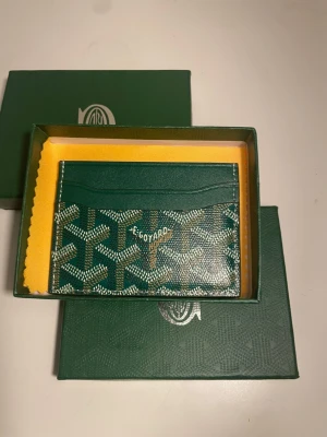 Grön Go4yard kortfodral - Snyggt och exklusivt kortfodral från Go4yard i grön färg med klassiskt mönster och vit logotyp. Fodralet har flera fack för kort och är tillverkat i läder. Perfekt för dig som vill ha något stilrent och lyxigt att bära dina kort i.