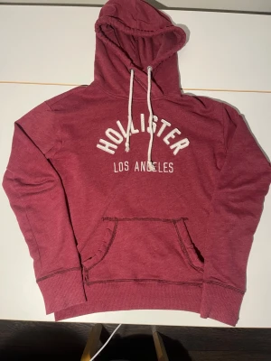 Vinröd hoodie från Hollister XS - Säljer en riktigt trendig vinröd hoodie från Hollister. Perfekt nu till sommaren. Skick 6/10 har ett hål vid fickan men inga andra defekter. Därav det billiga priset. 